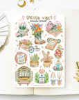 Premium Handmade Sticker Sheet Spring Vibes 105mm x 148mm - a sheet on the table with a white flower branch, an opened notebook