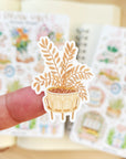 Premium Handmade Sticker Sheet Spring Vibes 105mm x 148mm - a piece on the finger and 2 sheets on the table with an opened notebook
