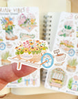 Premium Handmade Sticker Sheet Spring Vibes 105mm x 148mm - a piece on the finger and 2 sheets on the table with an opened notebook