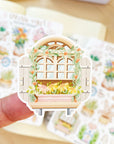 Premium Handmade Sticker Sheet Spring Vibes 105mm x 148mm - a piece on the finger and 2 sheets on the table with an opened notebook