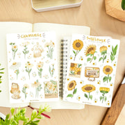 Premium Handmade Sticker Sheet Chamomile Sunflower 105mm x 148mm - 2 sheets on the table with a plant branch, an opened notebook