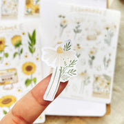 Premium Handmade Sticker Sheet Chamomile Sunflower 105mm x 148mm - a piece on the finger and 2 sheets on the table with an opened notebook
