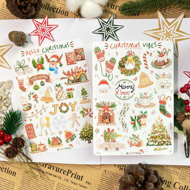 Premium Handmade Sticker Sheet Christmas 105mm x 148mm - 2 sheets on the table with an opened notebook, an acorn, 5 pinecones, 3 stars