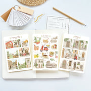 Premium Handmade Sticker Sheet Cozy Doors 105mm x 148mm - 3 sheets on the table with a pencil, an opened notebook, a chapter heading