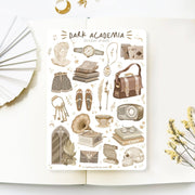 Premium Handmade Sticker Sheet Dark & Light Academia 105mm x 148mm - a sheet on the table with a white flower branch, an opened notebook