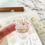 Premium Handmade Sticker Sheet Knitting Crochet 105mm x 148mm - a piece on the finger and a sheet on the table with a dark maroon flower branch, an opened notebook, a ruler