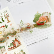 Premium Handmade Sticker Sheet Magical Cozy Winter 105mm x 148mm - 3 transparent pieces and a sheet on the table with an opened notebook