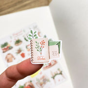Premium Handmade Sticker Sheet Magical Cozy Winter 105mm x 148mm - a piece and a sheet on the table with an opened notebook