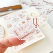 Premium Handmade Sticker Sheet Reading at Home 105mm x 148mm - a piece on the finger and a sheet on the table with a dark maroon flower branch, an opened notebook