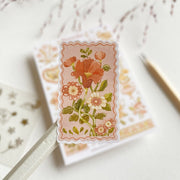 Premium Handmade Sticker Sheet Romantic Flower 105mm x 148mm - a piece and a sheet on the table with a pink flower branch in the background