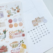 Premium Handmade Sticker Sheet Summer Breeze 105mm x 148mm - a piece above the calendar and a sheet on the table with a pencil, an opened notebook