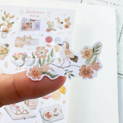 Premium Handmade Sticker Sheet Summer Breeze 105mm x 148mm - a piece on finger and a sheet on the table with an opened notebook