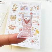Premium Handmade Sticker Sheet Summer Breeze 105mm x 148mm - a piece on the finger and a sheet on the table with an opened notebook