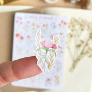 Premium Handmade Sticker Sheet Wild Flower 105mm x 148mm - a piece on the finger and a sheet on the table with a white flower branch, an opened notebook