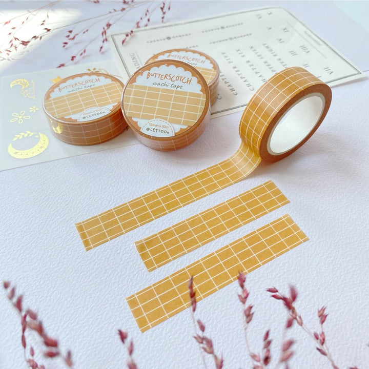 Premium Handmade Washi Tape Butterscotch Grid 15mm x 10m - 3 pieces and 4 washi tapes on the table with 2 dark maroon flower branches, a sticker sheet, a chapter heading