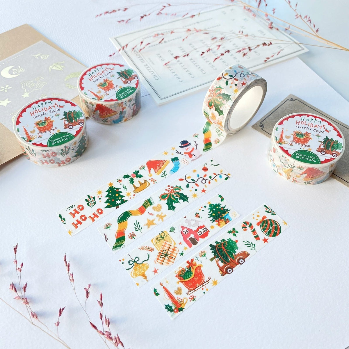 Premium Handmade Washi Tape Happy Holidays 20mm x 10m - 4 pieces and 4 washi tapes on the table with 2 dark maroon flower branches, a sticker sheet, a chapter heading, a notebook