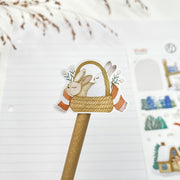 Fluffy Winter kiss-cut sticker on a pencil: two bunnies in a basket with a red scarf