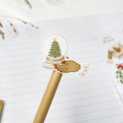 Slow Winter kiss-cut sticker on a pencil: a hand holding a snow globe with a Christmas tree