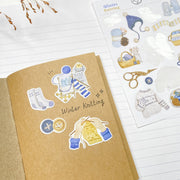 Winter Knitting stickers in a kraft notebook: socks, yarn, buttons and a knitted sweater