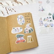 Winter Village stickers in a kraft notebook: a snowy house, skaters and a red car with a tree