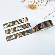Slow Winter washi tape roll, 15mm, unrolled next to three strips, on near-black with snowflakes: hands lighting a candle, hanging a bauble and writing letters