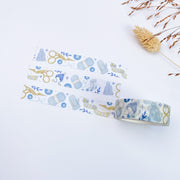 Winter Knitting washi tape roll, 15mm, unrolled next to three strips: in soft blue and mustard: stork scissors, cable-knit mittens, bobble hats and balls of yarn