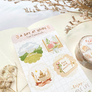 Premium Handmade Sticker Sheet A Day At Home 105mm x 148mm - a sheet on the table with a white flower branch, a purple flower branch, a washi tape, an opened notebook