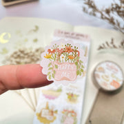 Premium Handmade Sticker Sheet A Day At Home 105mm x 148mm - a piece on the finger and a sheet on the table with a white flower branch, a purple flower branch, a washi tape, an opened notebook