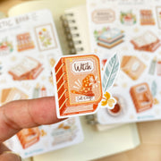 Premium Handmade Sticker Sheet Aesthetic Book 105mm x 148mm - a piece on the finger and 2 sheets on the table with an opened notebook