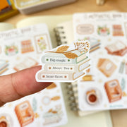 Premium Handmade Sticker Sheet Aesthetic Book 105mm x 148mm - a piece on the finger and 2 sheets on the table with an opened notebook