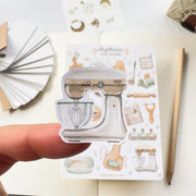 Premium Handmade Sticker Sheet Aesthetic Cozy Kitchen 105mm x 148mm - a piece on the finger and a sheet on the table with a pencil, an opened notebook