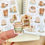 Premium Handmade Sticker Sheet Coffee 105mm x 148mm - a piece on the finger and 2 sheets on the table with an opened notebook