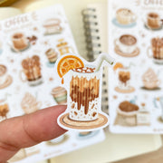 Premium Handmade Sticker Sheet Coffee 105mm x 148mm - a piece on the finger and a sheet on the table with an opened notebook