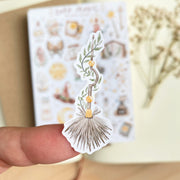 Premium Handmade Sticker Sheet Dark Magic 105mm x 148mm - a piece on the finger and a sheet on the table with a white flower branch, an opened notebook