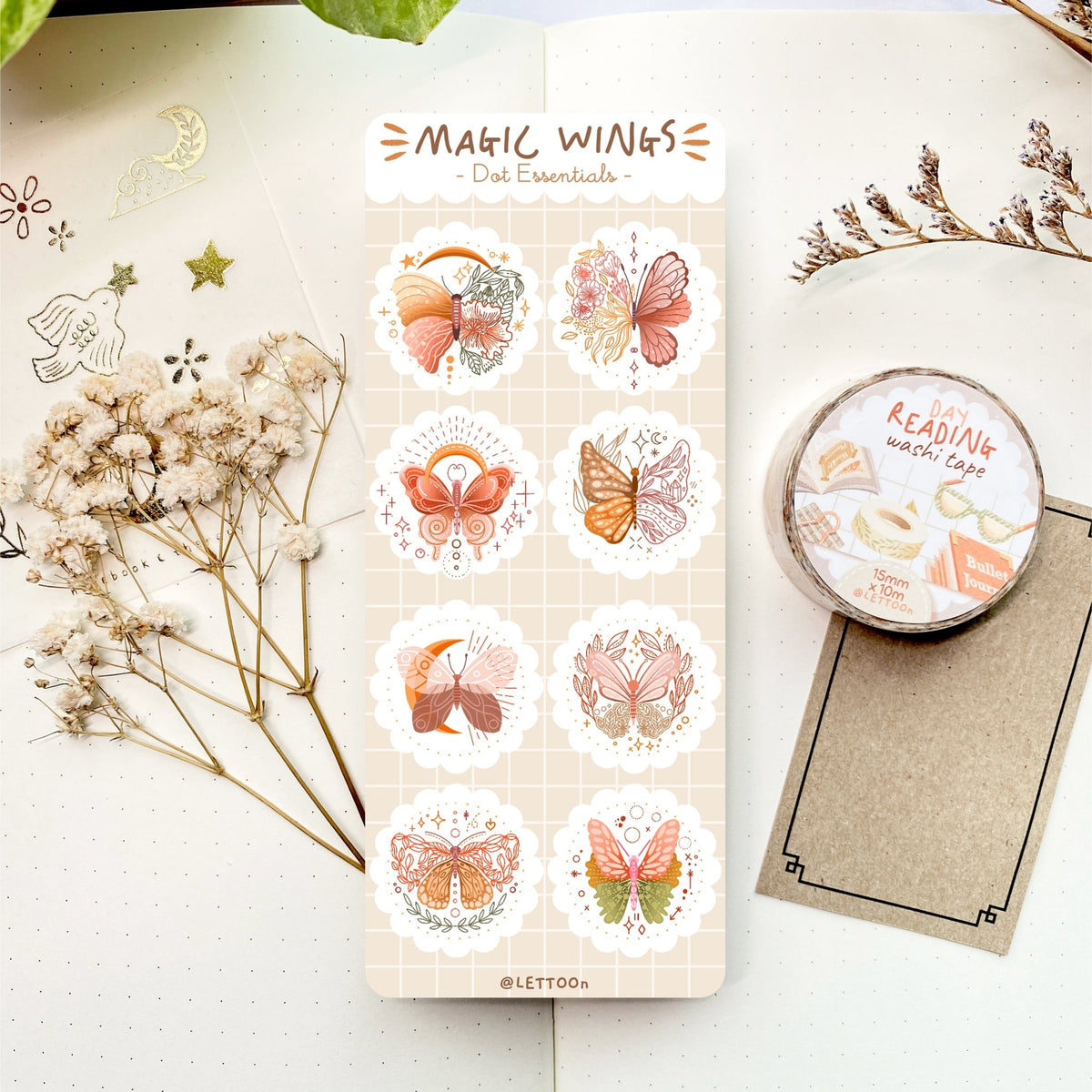 Premium Handmade Sticker Sheet Magic Wings 105mm x 148mm - a sheet on the table with a white flower branch, a purple flower brand, an opened notebook, a golden sticker sheet, a washi tape