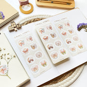 Premium Handmade Sticker Sheet Magic Wings 105mm x 148mm - 3 sheets on the table with a white branch, an opened notebook, a purple flower branch, a washi tape, a tape, a pen with box