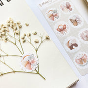 Premium Handmade Sticker Sheet Magic Wings 105mm x 148mm - a piece on the white flower branch and a sheet on the table 