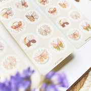 Premium Handmade Sticker Sheet Magic Wings 105mm x 148mm - 2 sheets on the table with a purple flower branch, an opened notebook