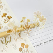 Premium Handmade Sticker Sheet Mellow Flower 105mm x 148mm - 3 pieces on the stick and a piece on the finger and a sheet on the table with an opened notebook