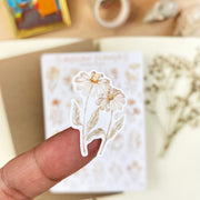 Premium Handmade Sticker Sheet Mellow Flower 105mm x 148mm - a piece on the finger and a sheet on the table with a white flower branch, an opened notebook