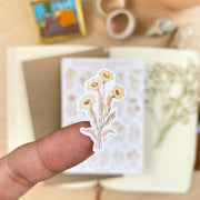 Premium Handmade Sticker Sheet Mellow Flower 105mm x 148mm - a piece on the finger and a sheet on the table with a white flower branch, an opened notebook