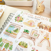 Premium Handmade Sticker Sheet Spring Garden 105mm x 148mm - a sheet on the table with a rabbit statue, an opened notebook