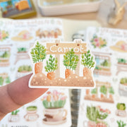 Premium Handmade Sticker Sheet Spring Garden 105mm x 148mm - a piece on the finger and 2 sheets on the table with a rabbit statue, an opened notebook