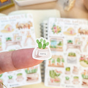 Premium Handmade Sticker Sheet Spring Garden 105mm x 148mm - a piece on the finger and 2 sheets on the table with a rabbit statue, an opened notebook