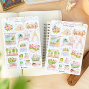 Premium Handmade Sticker Sheet Spring Garden 105mm x 148mm - 2 sheets on the table with a rabbit statue, an opened notebook