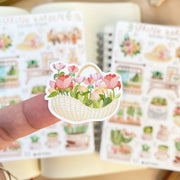 Premium Handmade Sticker Sheet Spring Garden 105mm x 148mm - a piece on the finger and 2 sheets on the table with an opened notebook