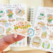Premium Handmade Sticker Sheet Spring Vibes 105mm x 148mm - a piece on the finger and 2 sheets on the table with an opened notebook